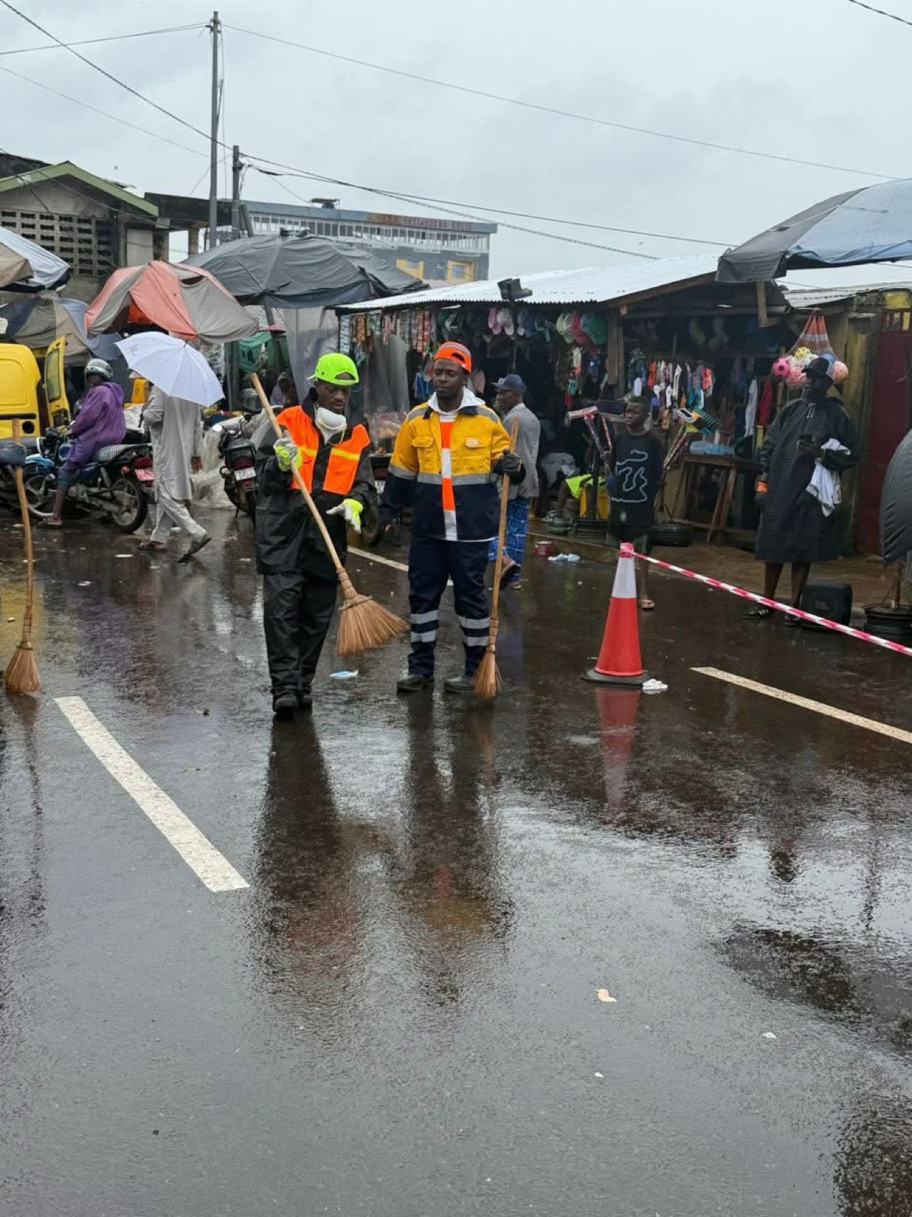 Le Mélangeur balayant une rue en tenue de chantier, avec les habitants