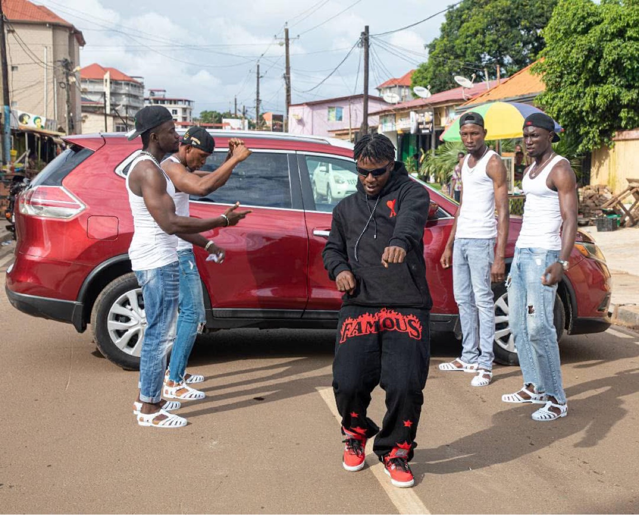Le Mélangeur dansant dans une rue de Conakry devant un SUV rouge, entouré de danseurs