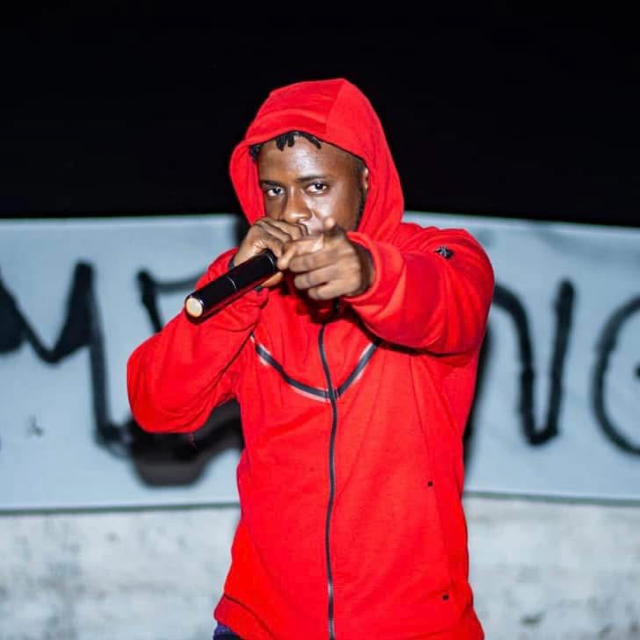 Le Mélangeur sur scène en hoodie rouge, micro en main, le doigt pointé vers l’objectif